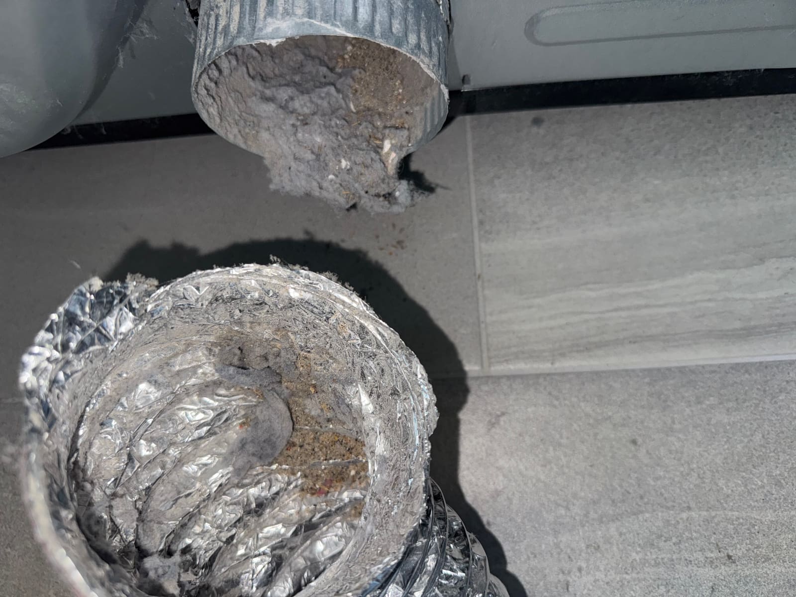 A section of dryer duct laid on the floor with its interior lined in compacted lint and grey debris.