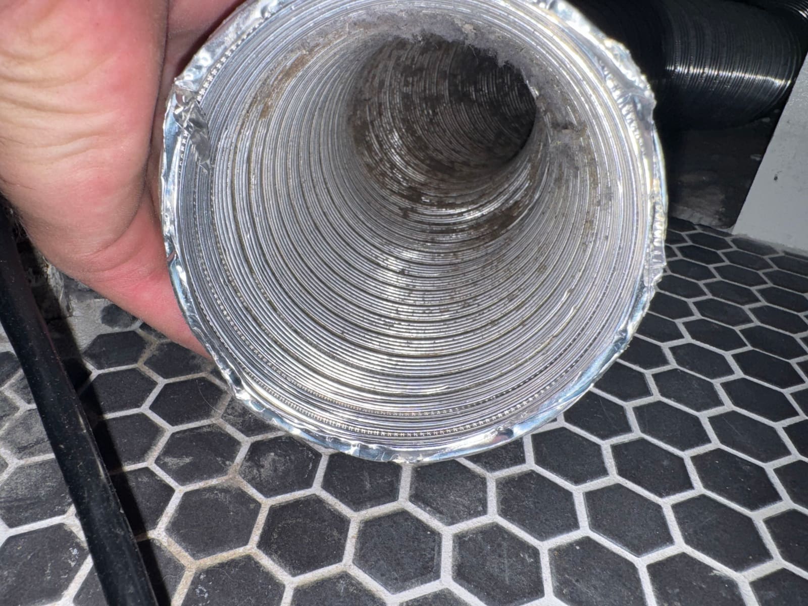 A cleaned flexible dryer duct held up to the light, showing bare metal ribbing along its full length.