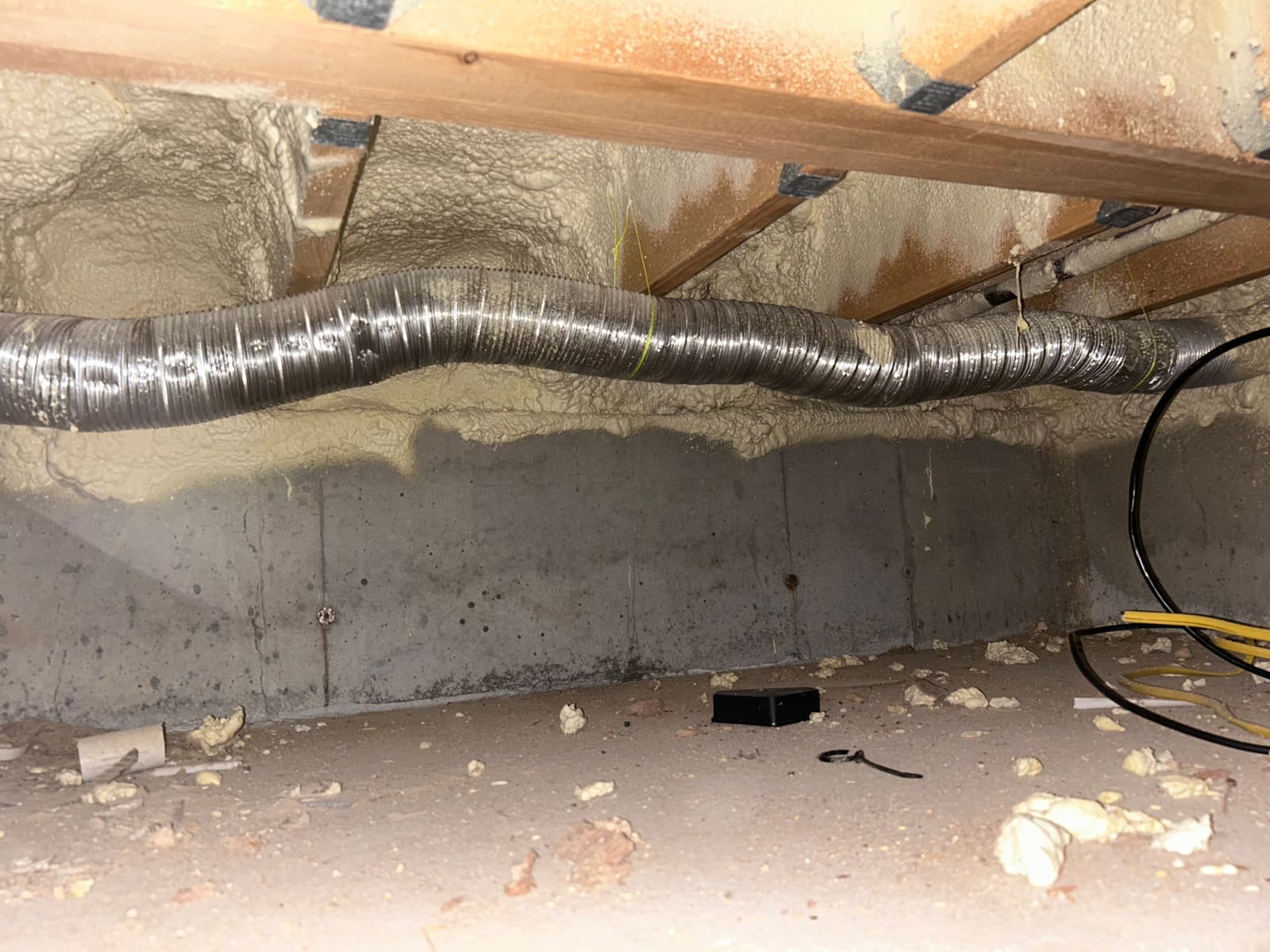 A rigid metal dryer duct run installed along a crawlspace foundation wall, supported and sealed to code.