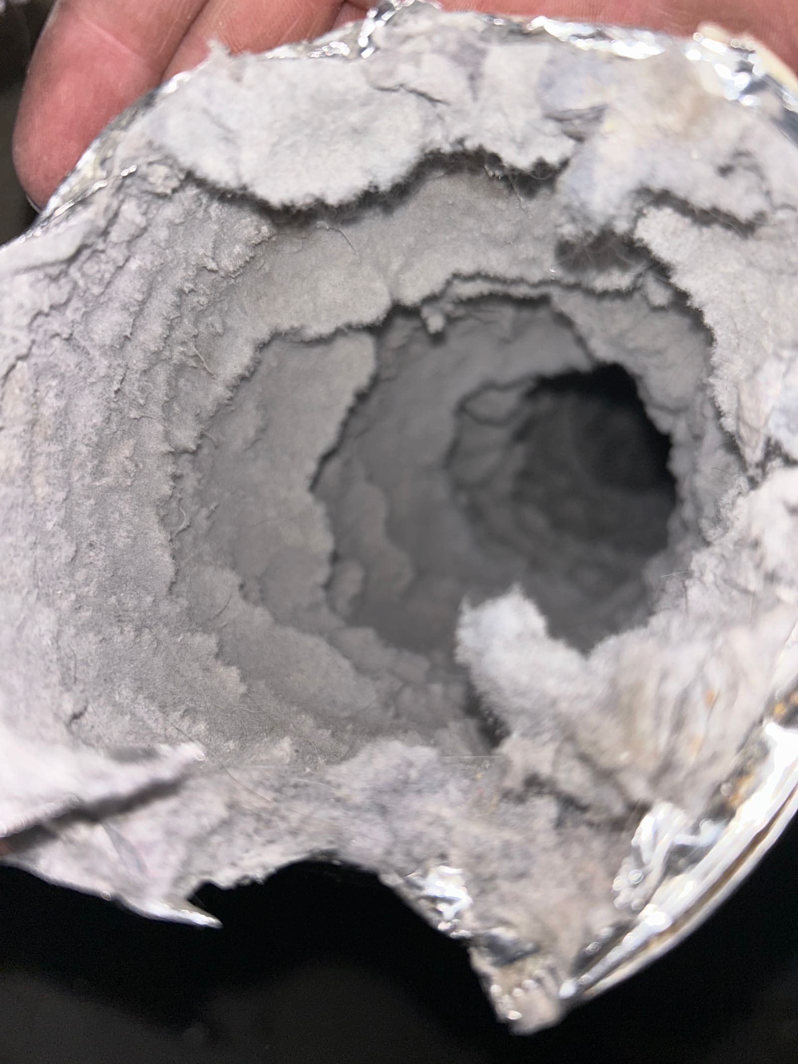 A flexible dryer duct held open in one hand, its inside walls lined with thick felted lint that has closed the opening down to a small dark hole.