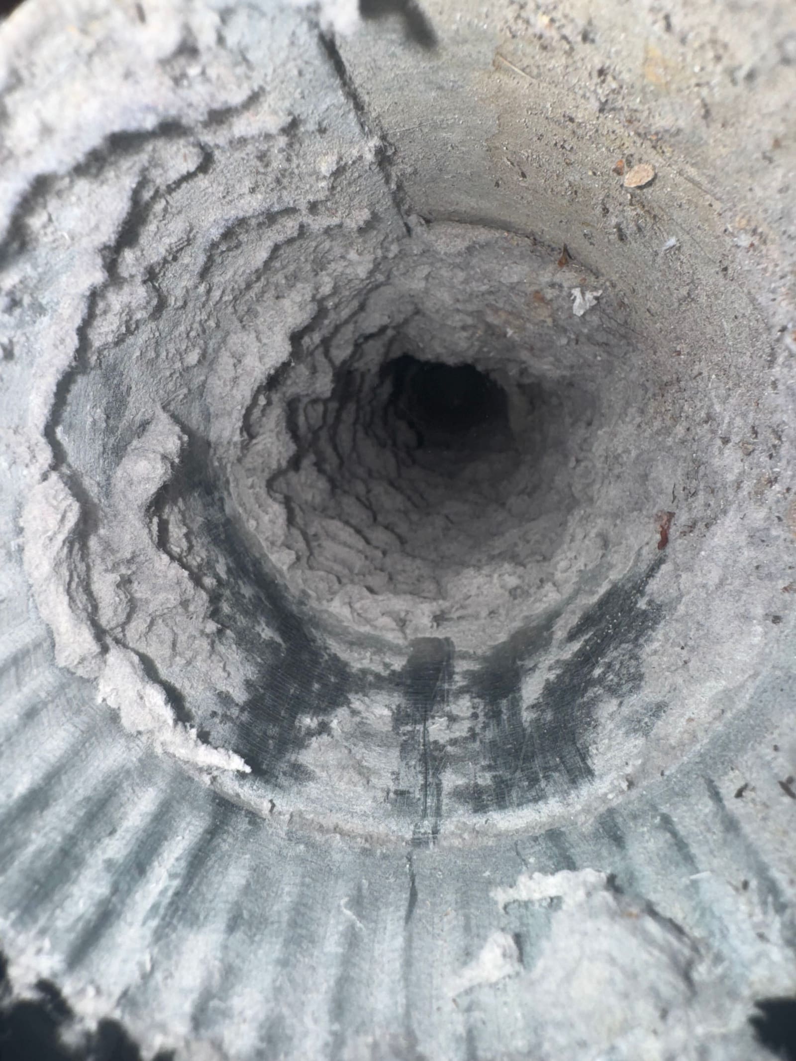Inside a dryer duct caked with a thick felted layer of lint, leaving an opening a fraction of the duct’s full diameter.