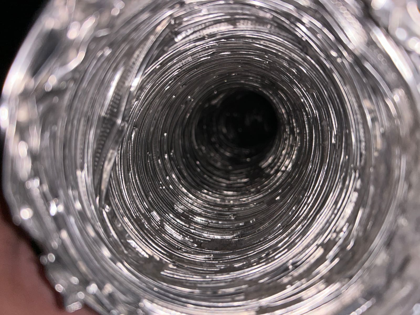The same flexible dryer duct after cleaning, looking straight down a clear run with the bare metal ribbing visible the whole way.