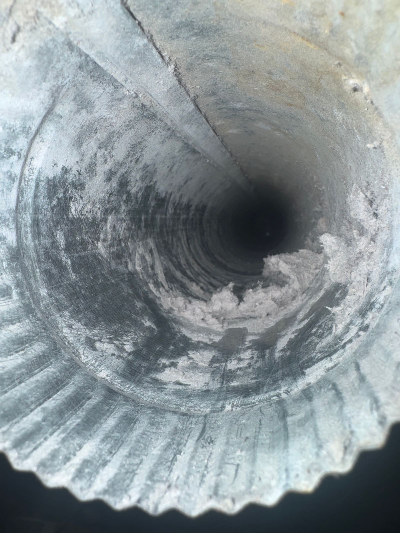 Interior of a ribbed dryer duct lined with lint and dark residue, the passage narrowed to a fraction of its width.